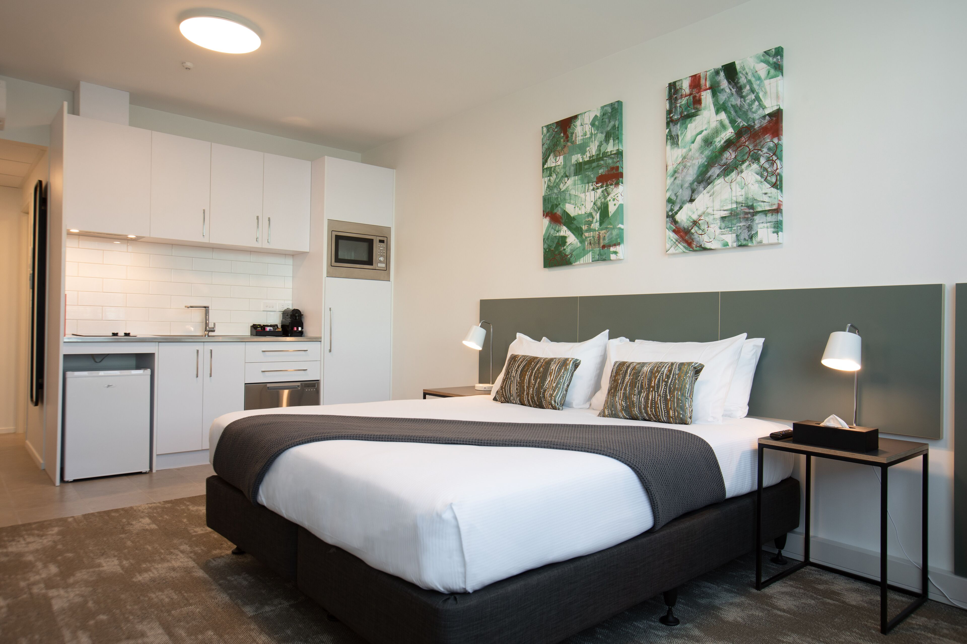 Quarto de hotel moderno com uma cama grande, uma kitchenette pequena e obras de arte nas paredes.
