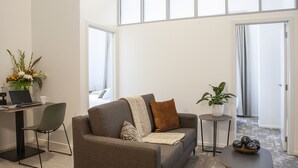 Una sala de estar moderna con un sofá, una mesita, un escritorio con una computadora portátil y una planta en maceta.