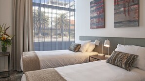 Habitación de hotel con dos camas, una mesita de noche con lámpara y una obra de arte en la pared.
