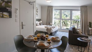 Una habitación de hotel moderna con comedor, sofá y una ventana grande con vista a palmeras.