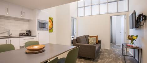 A modern kitchen with white cabinets, a microwave, and a dining area with a table and chairs.