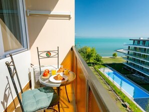 Een balkon met een ontbijtje, een stoel en uitzicht op een modern gebouw en een zwembad.