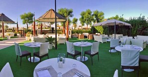 An outdoor dining area with round tables and chairs, a gazebo, and greenery. - Nautico (Riccione)