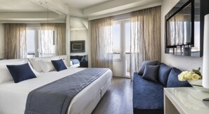 A modern hotel room with a large bed, a sofa, a desk, and a balcony with curtains. - Nautico (Riccione)