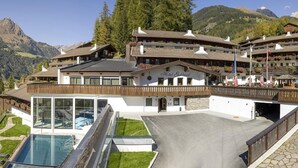 A hotel with a modern glass pool, surrounded by a well-maintained lawn and a mountain backdrop. - Cosy apartment with own sauna in hotel (Matrei in Osttirol)