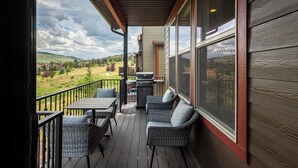 Une terrasse extérieure couverte, équipée d’une table et de chaises, d’un barbecue et offrant une vue sur un paysage vallonné.