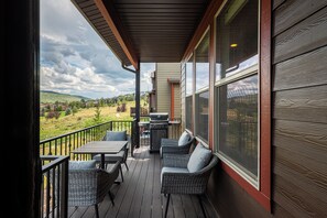 Una terrazza esterna coperta con tavolo e sedie, un barbecue e vista su un paesaggio collinare.