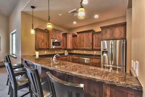 A kitchen with granite countertops, stainless steel appliances, wooden cabinets, and bar seating.