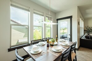 Un comedor con una mesa de madera dispuesta para cuatro, ventanas amplias y vistas al exterior.