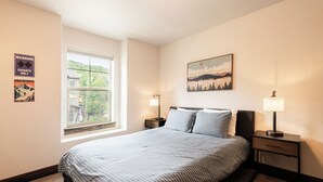 Une chambre à coucher avec un lit, deux tables de chevet, une fenêtre et un tableau au mur.
