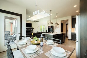 A modern kitchen with a central island, dining area with set tables, and a view to the outside.