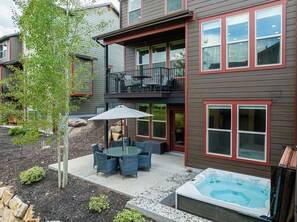 A two-story house with a patio area featuring outdoor furniture and a hot tub.