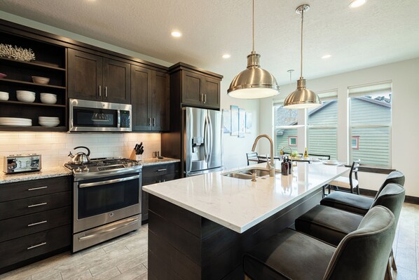 A modern kitchen with dark cabinetry, stainless steel appliances, a central island with seating, and pendant lighting.