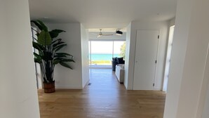 Un pasillo amplio con suelo de madera que conduce a un balcón con vista al mar.