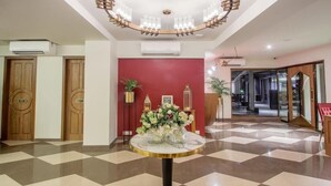 A lobby with a checkered floor, a central round table with a vase of flowers, wooden doors, and a red accent wall. - T24 Retro (Mumbai)
