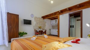 A hotel room with a bed, a TV, a stone wall, a kitchen, and a wooden ceiling. - Apartment Klara (Dubrovnik)
