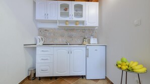 A compact kitchen with white cabinets, a stone backsplash, and a small refrigerator. - Apartment Klara (Dubrovnik)