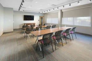 A conference room with a long table, multiple chairs, water bottles, a flat-screen TV, and a large window. - Aloft by Marriott Lubbock (Lubbock)
