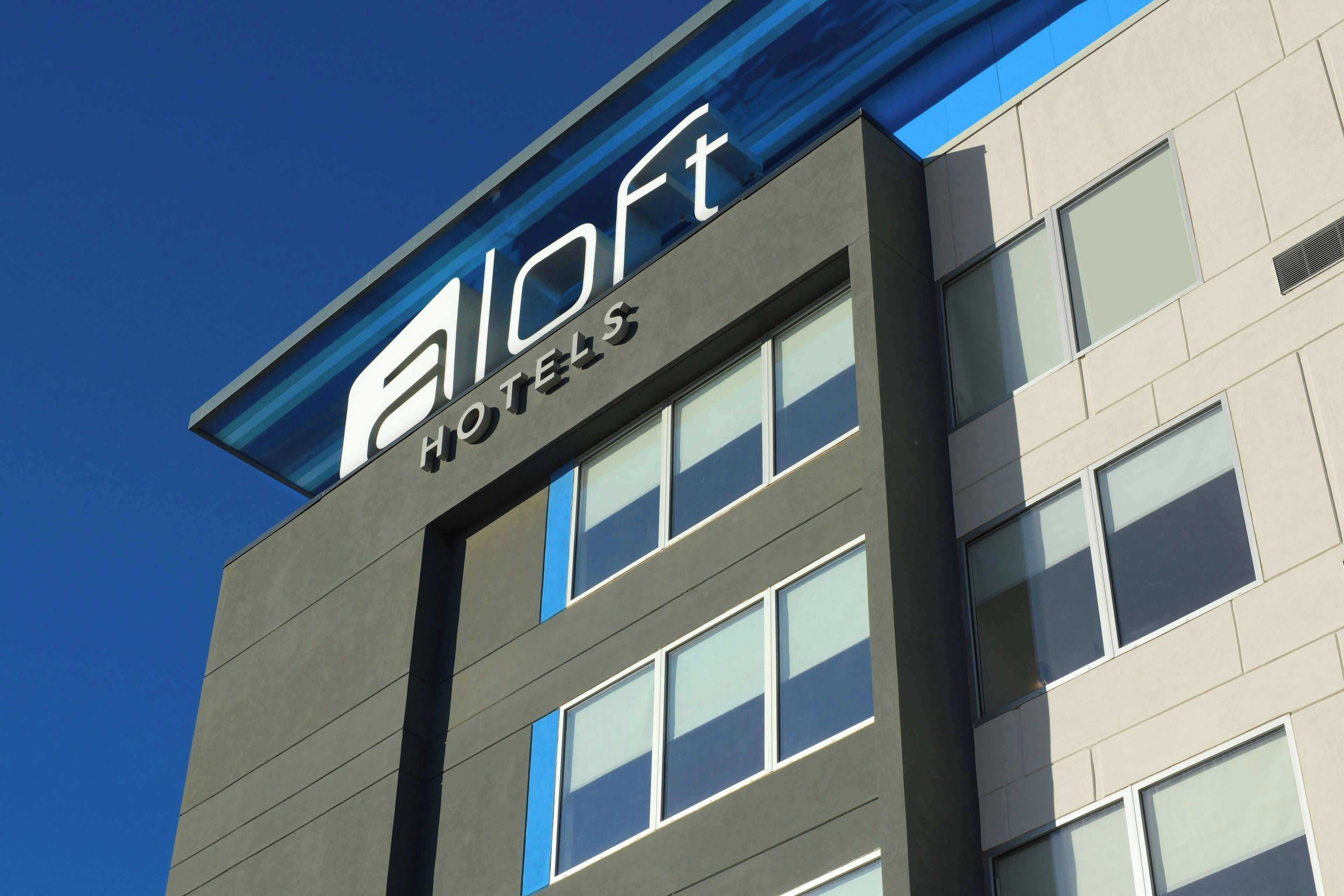 A modern hotel building with a prominent logo and name on the facade.