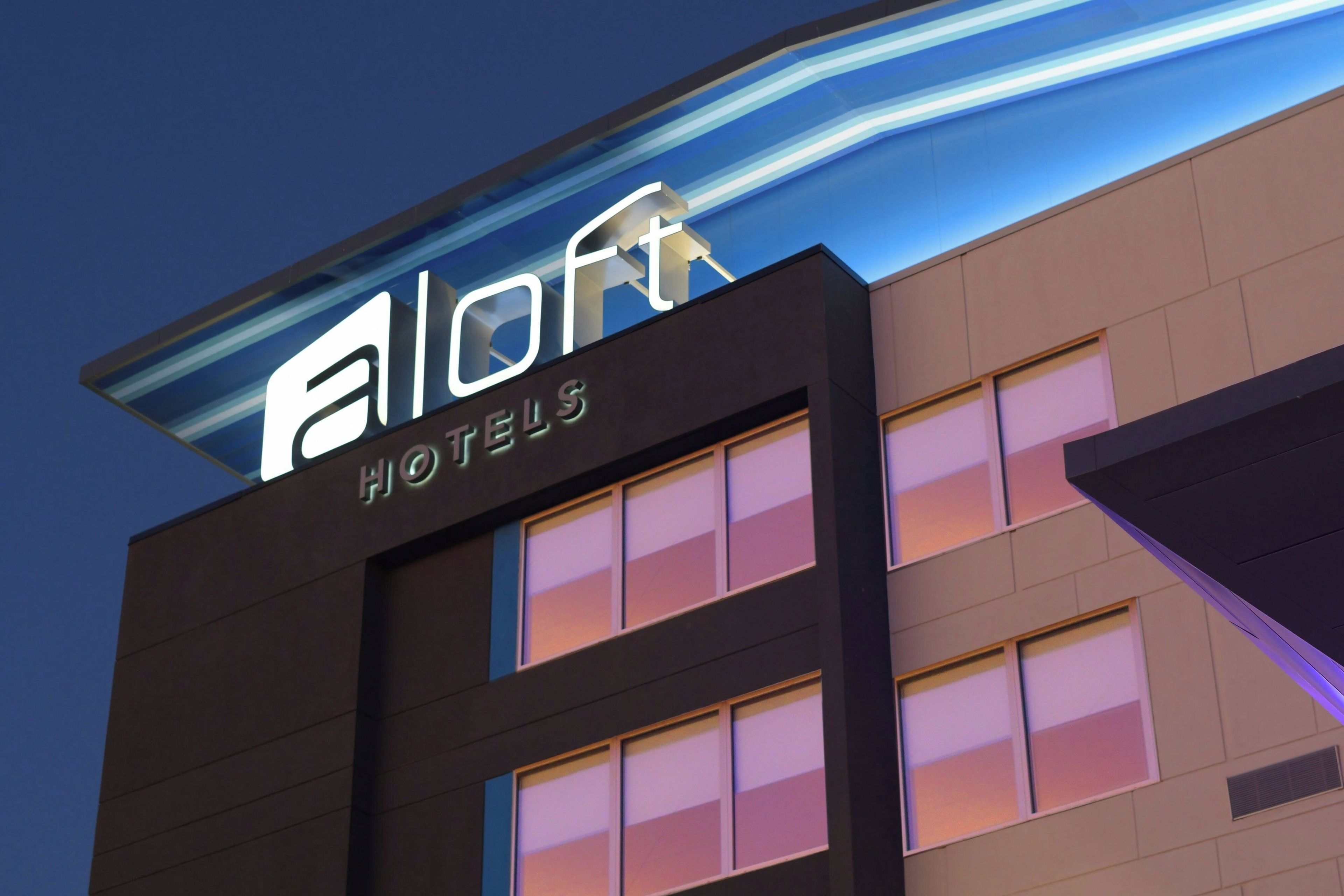 A hotel sign with the name 'Allo Hotels' illuminated against a twilight sky.