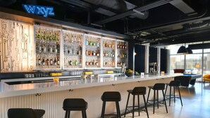 A bar area with a neon sign, shelves of bottles, and bar stools. - Aloft by Marriott Lubbock (Lubbock)