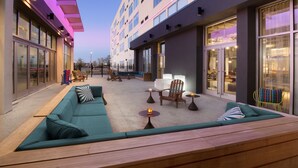 A modern outdoor seating area with a sofa, chairs, and tables, surrounded by glass doors and windows. - Aloft by Marriott Lubbock (Lubbock)