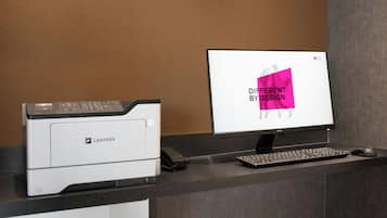 A printer, a monitor, and a keyboard on a desk with a corkboard wall.