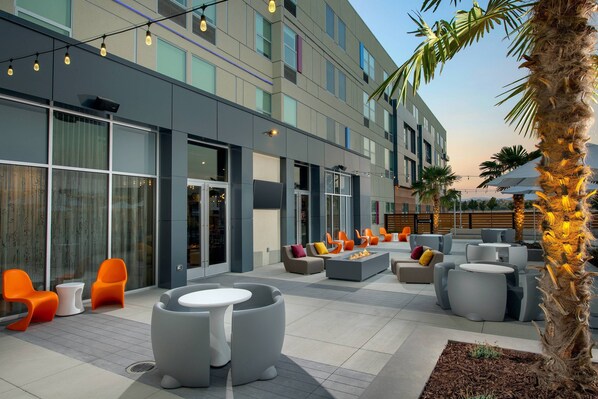 An outdoor seating area with modern furniture, a palm tree, and a building with large windows and a balcony. - Aloft by Marriott Lubbock (Lubbock)