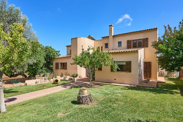 A modern two-story house with a well-maintained lawn and a tree in the front yard. - Garrovers de Shorta, holiday home with Pool, Large Garden, and Countryside Views (S'Horta)