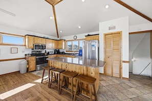 A kitchen with wooden cabinets, a stainless steel refrigerator, a microwave, and a large island with stools. - Sunbelievable | 930 ft from the beach | Private Pool, Hot Tub, Dog-Friendly | Corolla (Corolla)