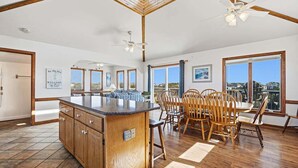 Cocina amplia con una isla grande, mesa de comedor de madera y sillas, con ventanas grandes que ofrecen una vista.