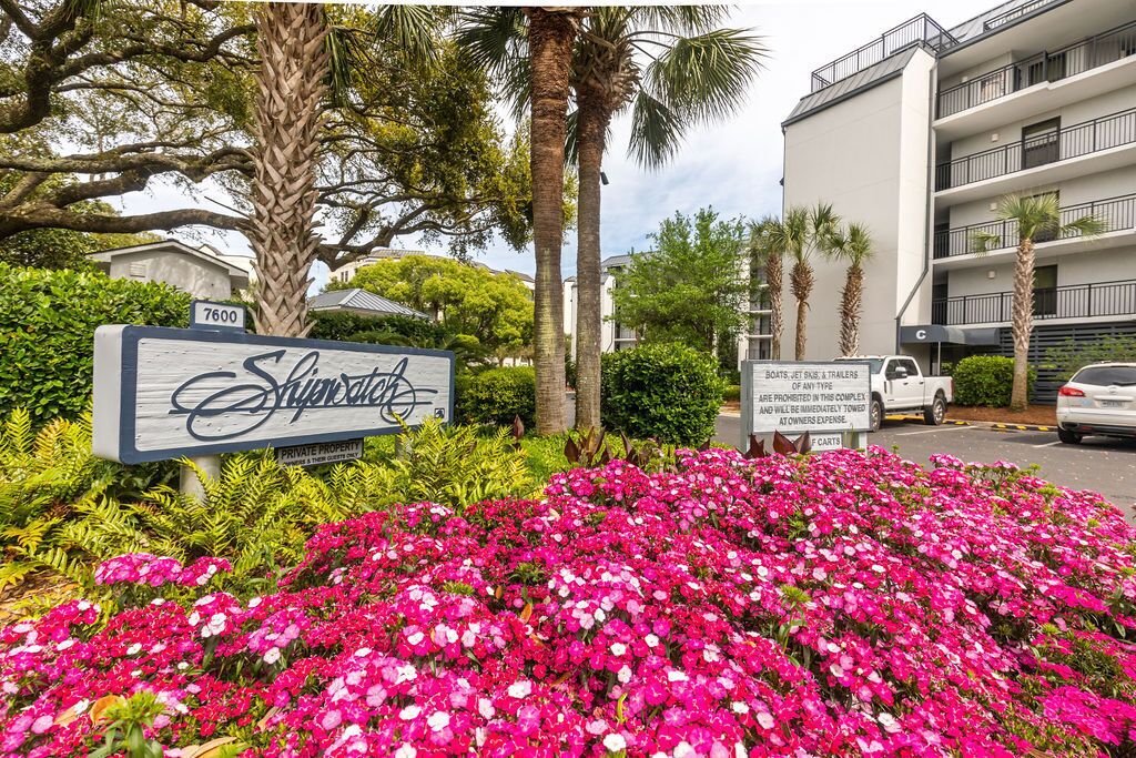 A hotel entrance with a sign, a flower bed, and a parking area.