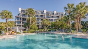 A hotel with a pool, palm trees, and lounge chairs.