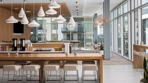 A modern kitchen with a long island, bar stools, hanging pendant lights, and a view of the city through large windows. - Element by Marriott Tampa Midtown (Tampa)
