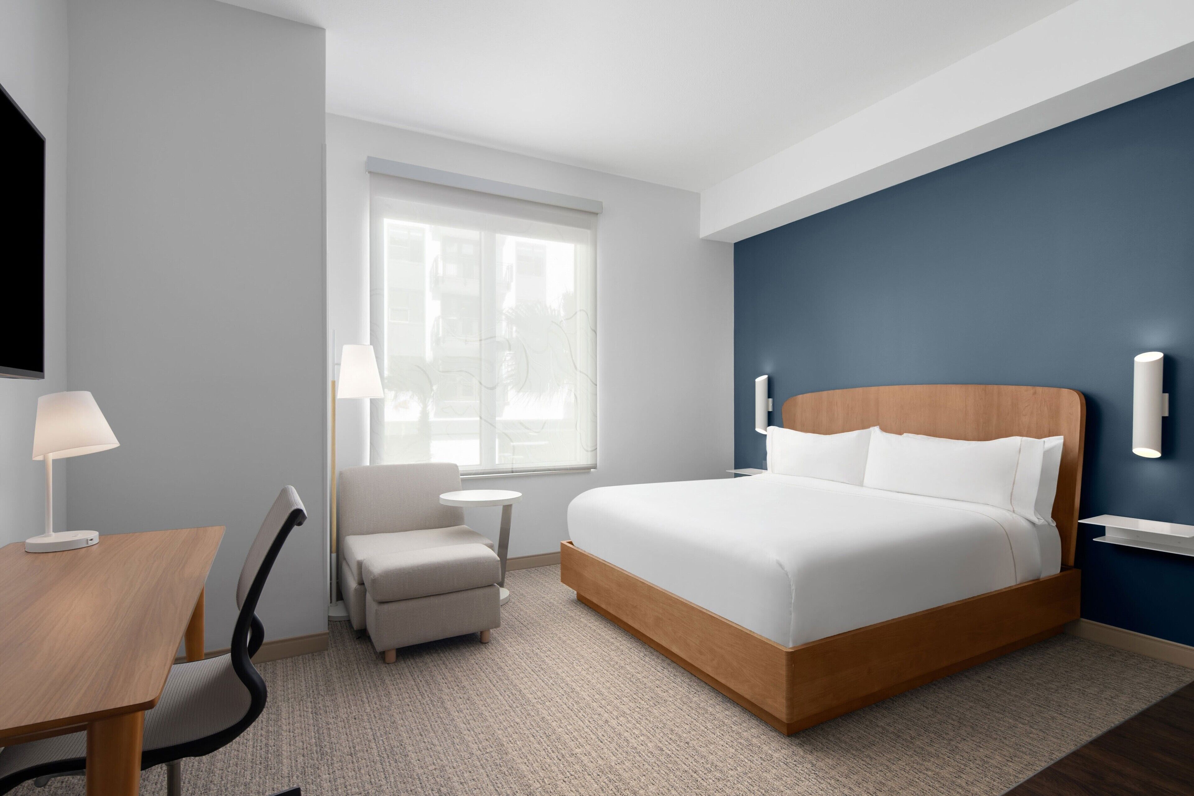 Una habitación de hotel con cama, escritorio, silla, mesita y ventana.
