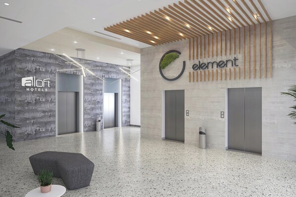 A modern hotel lobby with a terrazzo floor, a reception desk, and a large logo on the wall.