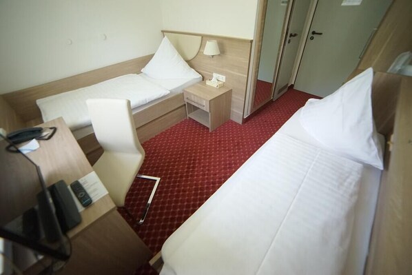 A hotel room with two beds, a desk, a chair, a nightstand, and a red carpeted floor. - Aparthotel Wangener Landhaus (Stuttgart)