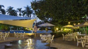 An outdoor patio area with tables and chairs, a water feature, and umbrellas providing shade. - Gamma Cuernavaca Puerta Paraiso (Cuernavaca)