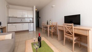 Ett modernt kök med vita skåp, en matplats med ett träbord och stolar, en tv och en vinflaska på en matta.