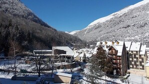 A snow-covered mountain town with traditional buildings and a modern hotel. - Cozy Studio for 2, South Balcony, at Gondola Foot, Parking, WiFi, Pets Welcome (Bagnères-de-Luchon)