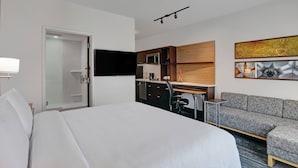 A modern hotel room with a large bed, a desk with a computer, a sofa, a flat-screen TV mounted on the wall, and a microwave in the kitchenette. - TownePlace Suites by Marriott Columbus Dublin (Dublin)