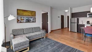 A modern living room with a grey sofa, a small table, and a kitchen area with a fridge and microwave. - TownePlace Suites by Marriott Columbus Dublin (Dublin)