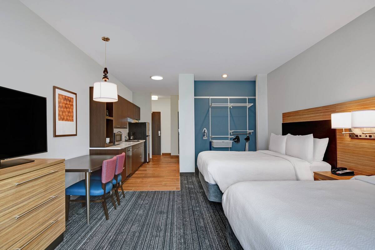 Habitación de hotel con dos camas, un escritorio con silla, televisión y kitchenette.