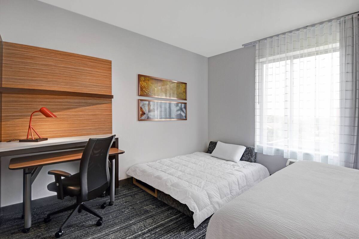 Una habitación de hotel con una cama, un escritorio con una silla, una lámpara roja y obras de arte en la pared.