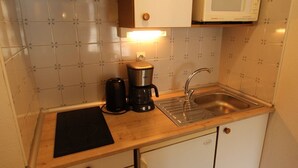 Una kitchenette compacta con microondas, cafetera y lavabo.