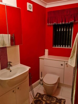 A bathroom with a red wall, a white sink, a toilet, and a window with a red curtain. - Luxurious, Stunning Detached Bungalow in Derby (Derby)