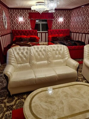 A room with a white leather sofa, red upholstered chairs, a chandelier, and patterned wallpaper. - Luxurious, Stunning Detached Bungalow in Derby (Derby)