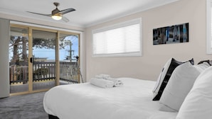 Ein Schlafzimmer mit einem Bett, einem Deckenventilator, einem Fenster mit Jalousien und einem Balkon mit Blick.