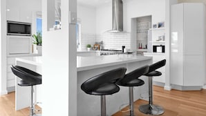 Eine moderne Küche mit weißen Schränken, einer Edelstahl-Dunstabzugshaube, einer Mikrowelle und einer Bar mit Hockern.