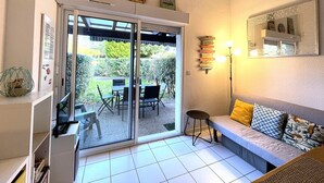 A room with a sliding glass door leading to a patio with a table and chairs. There is a sofa with cushions and a floor lamp. Decorative signs are on the wall. - T2 Apartment mezzanine with terrace and pets allowed (Soustons)